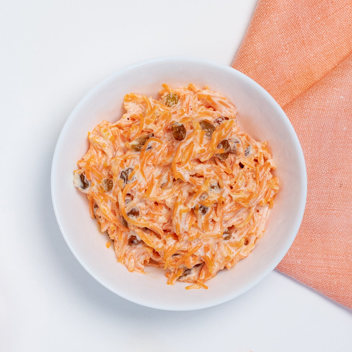 Creamy Carrots and Raisins Salad with shredded carrots and golden raisins in a white bowl by Zina's Fine Foods