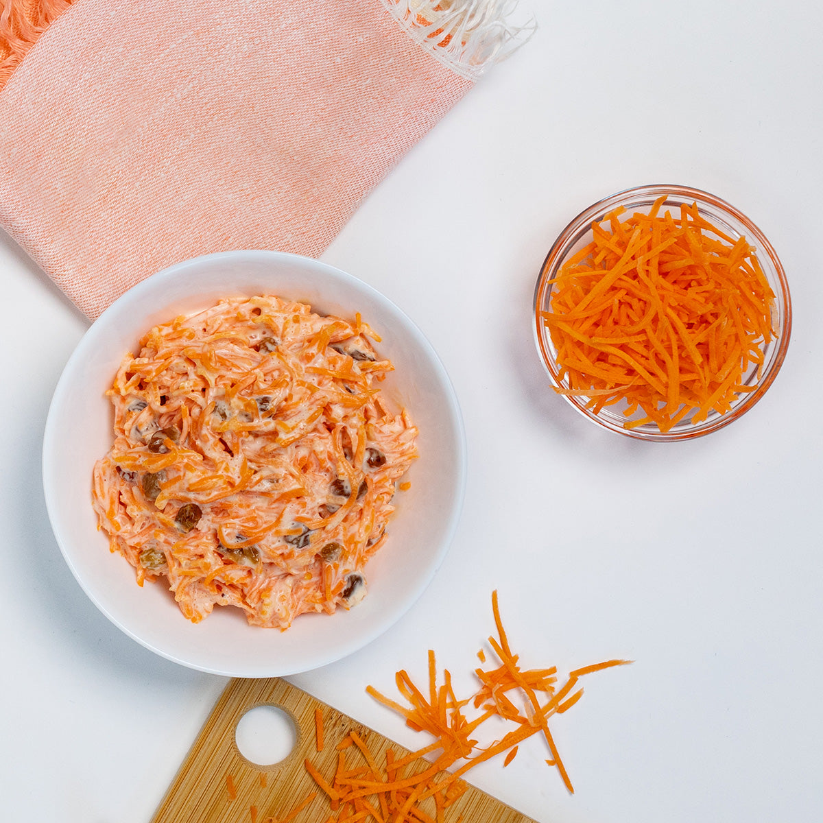 Zina's Fine Foods Carrots and Raisins Salad styled with fresh shredded carrots on a cutting board
