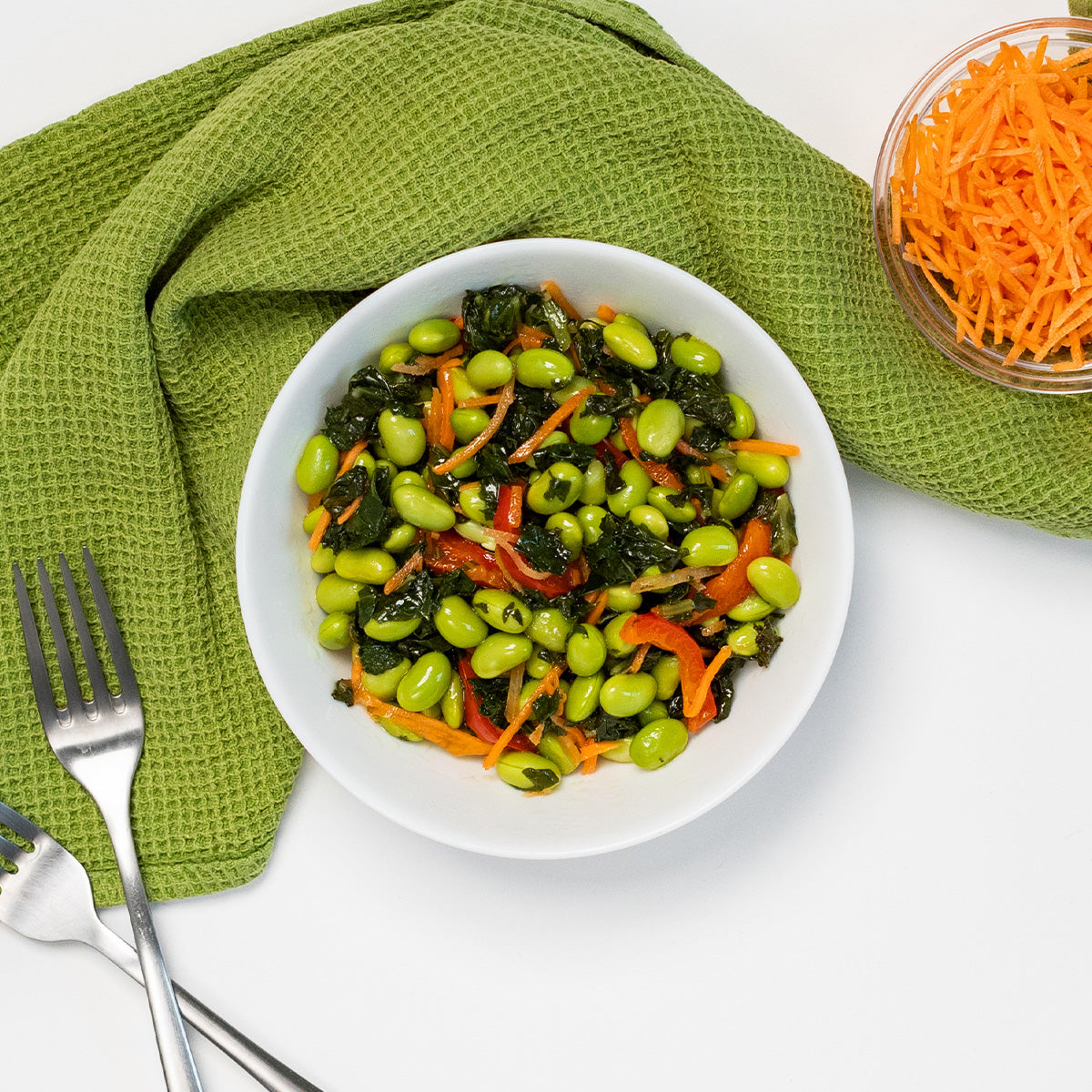 Edamame Kale Salad with edamame, sauteed kale, shredded carrots and red pepper in a white bowl by Zina's Fine Foods