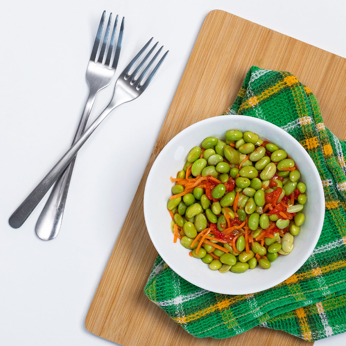 Zina's Fine Foods Edamame Salad with edamame and roasted peppers styled with forks on a bamboo board