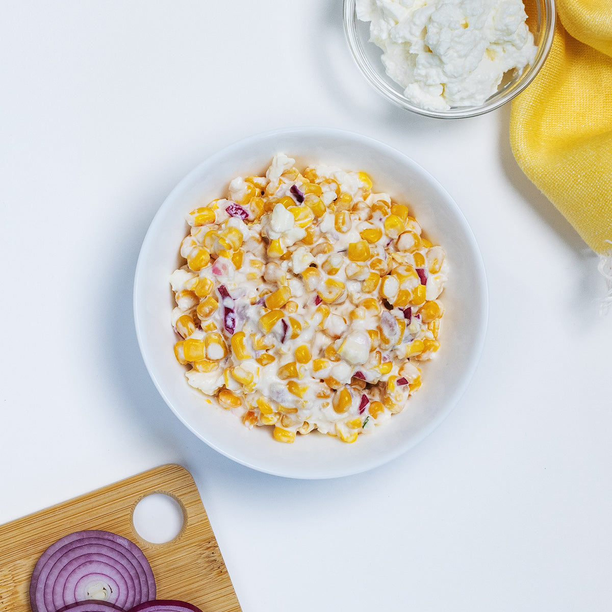 Mexican Street Corn Salad with sweet corn, red onion and cheese in a white bowl by Zina's Fine Foods