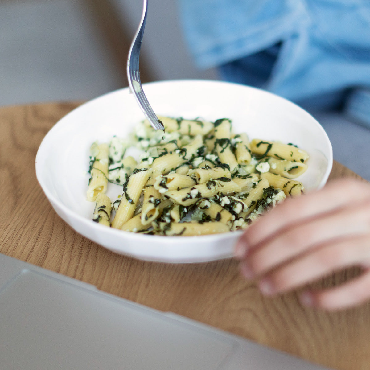 Person enjoying Zina's Fine Foods Penne Pasta with Spinach and Feta from a white bowl