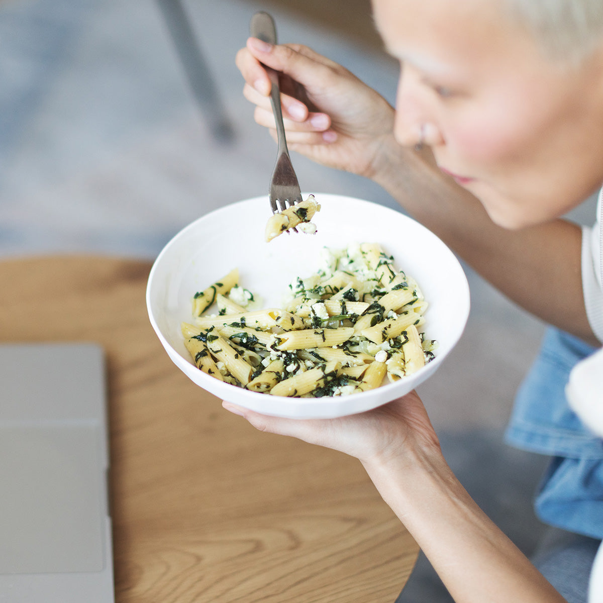 Woman lifting a forkful of Zina's Fine Foods Penne Pasta with Spinach and Feta from a white bowl
