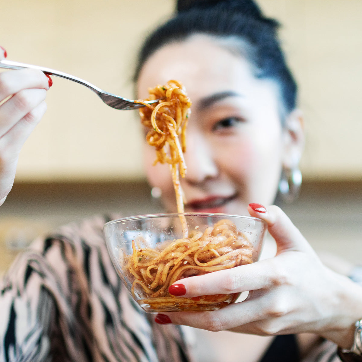 Woman lifting a forkful of Zina's Fine Foods Sesame Noodle Salad from a clear bowl