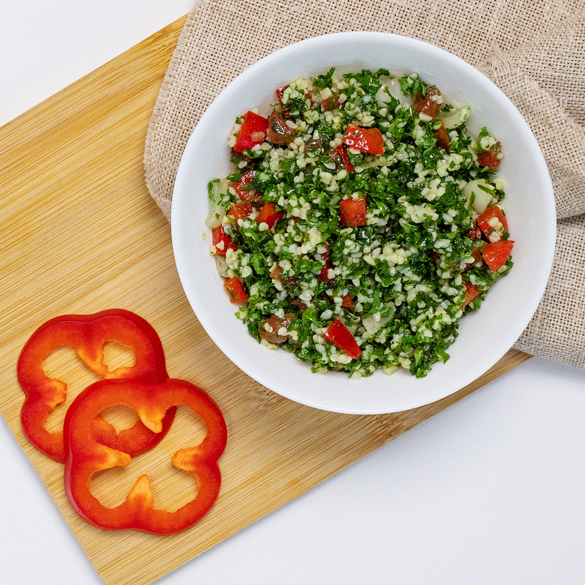 Zina's Fine Foods Tabbouleh Salad styled with red bell pepper slices on a bamboo board