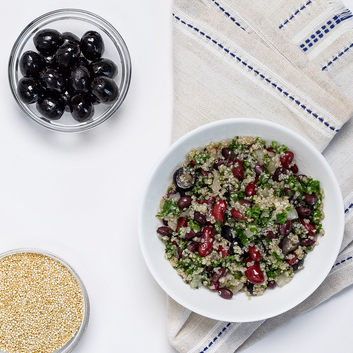 Zina's Fine Foods Vegan Quinoa Salad styled with side bowls of black olives and raw quinoa