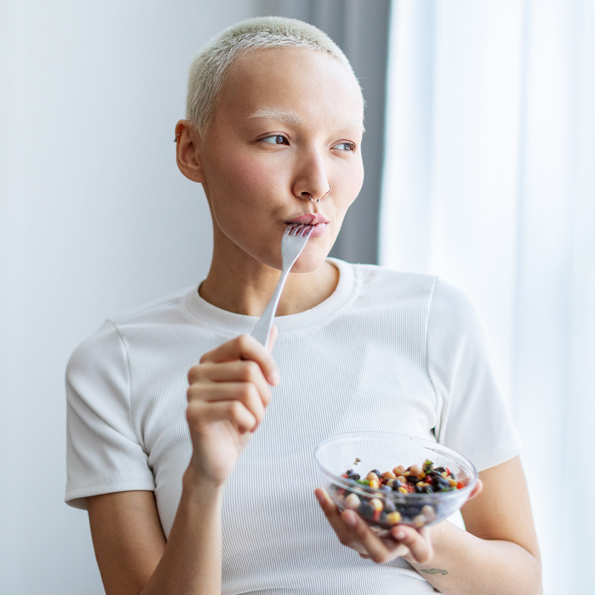 Woman in white t-shirt eating Zina's Fine Foods Black Bean Salad from a clear glass bowl